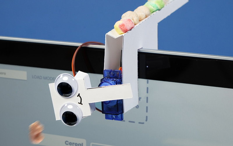 A smiling diy cardboard robot sitting on top of a webcam